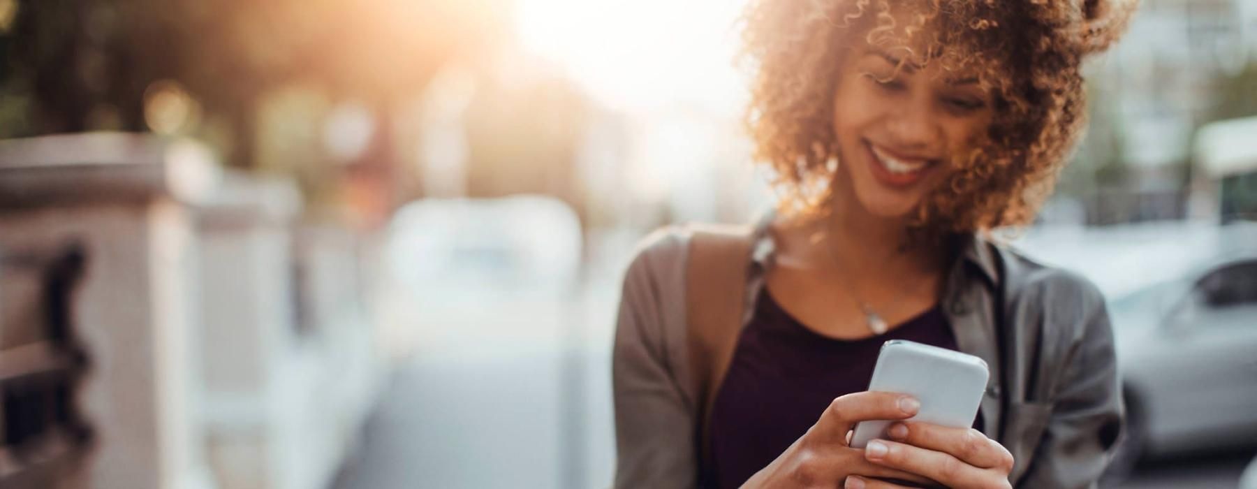 woman texts on her phone as she walks through the city